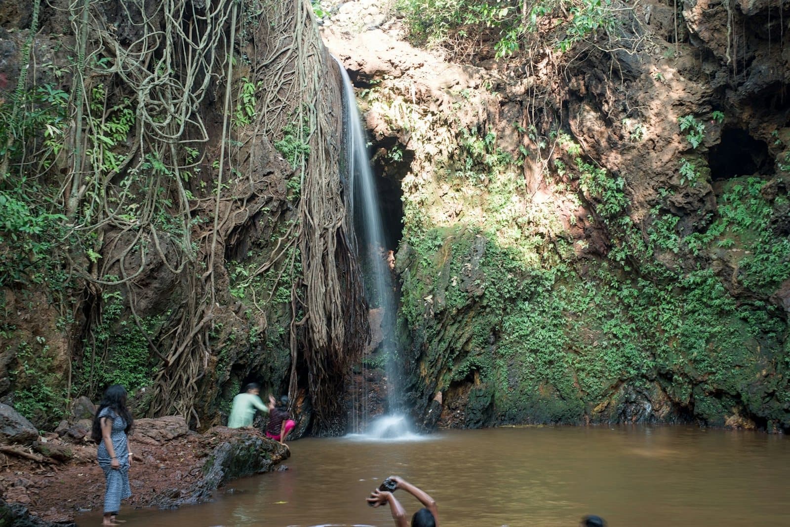 A waterfall dropping into a plunge pool with swimmers at its edge
