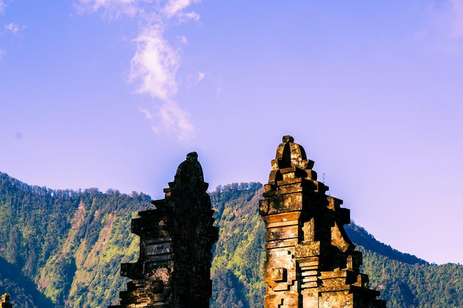 A split temple gate of dark volcanic stone against a mountain ridge at dusk