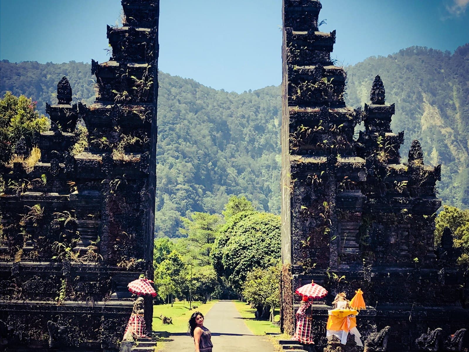 The Handara gate, two tall stone towers either side of the resort road, a visitor posing in the gap with forested hills behind