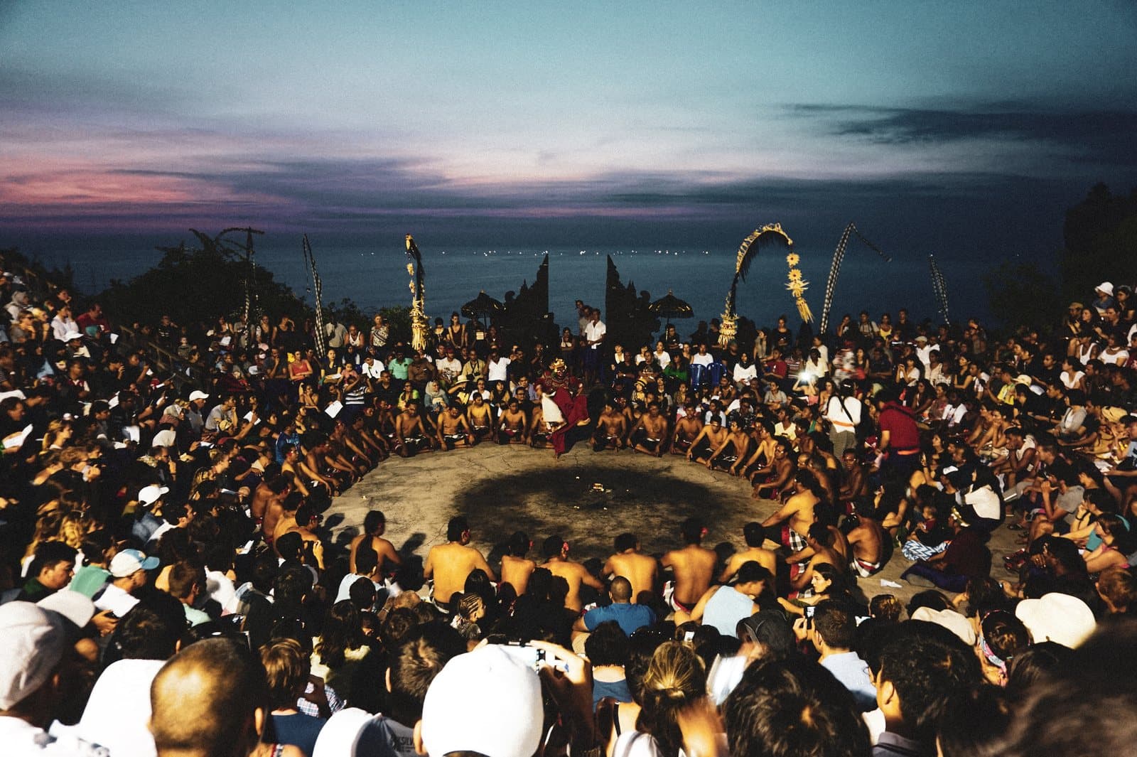 The Kecak amphitheatre at Uluwatu at dusk, the chanting circle at its centre and the ocean behind