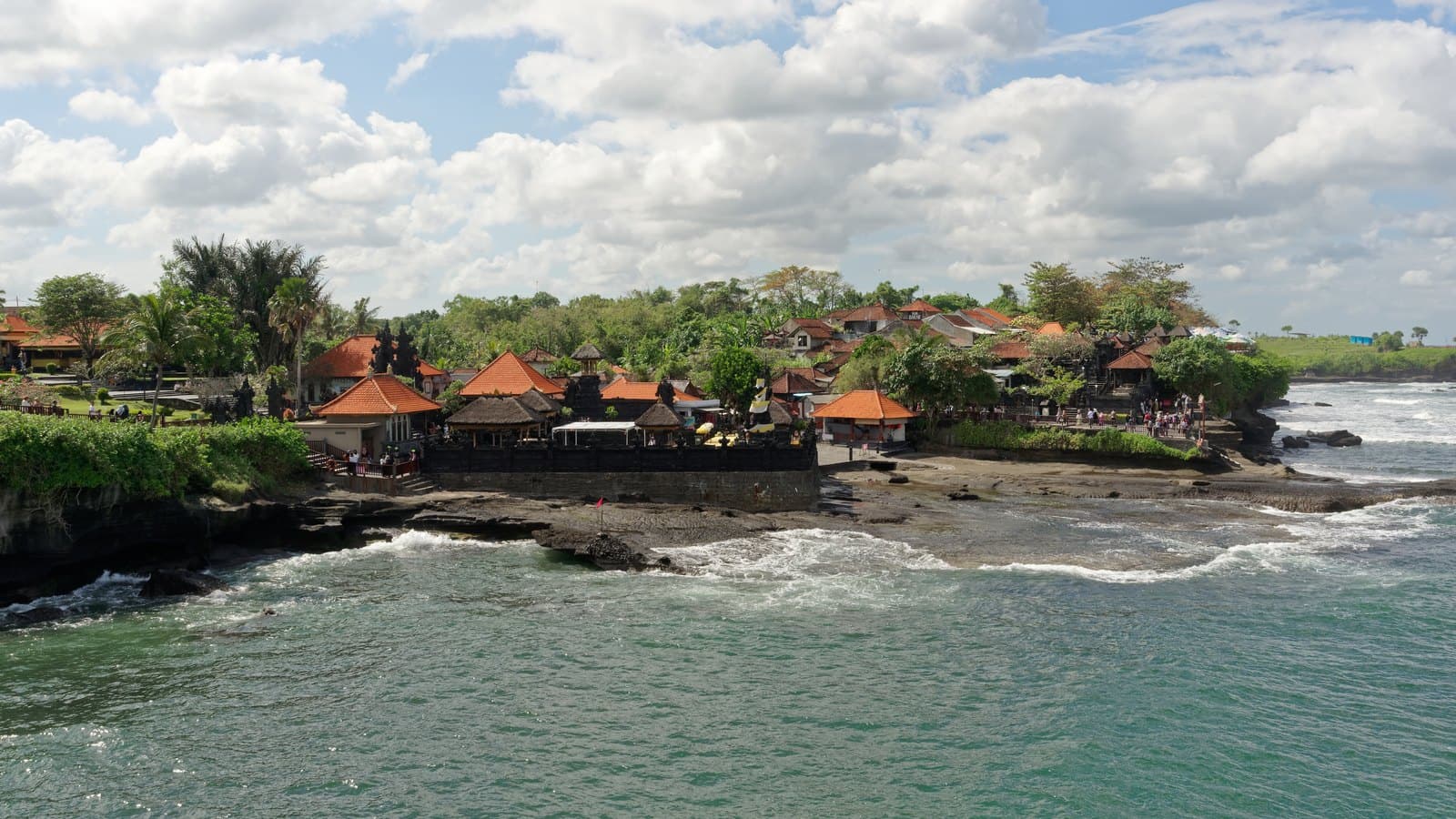 The Tanah Lot headland at low tide, the rock shelf below the temple exposed and the surf breaking beyond it