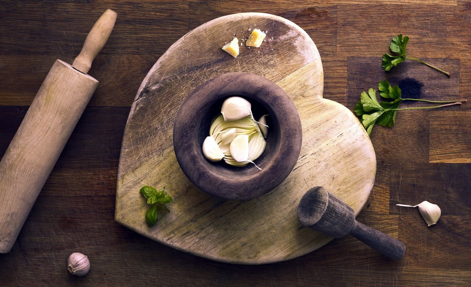 A stone mortar and pestle with garlic and aromatics on a wooden board