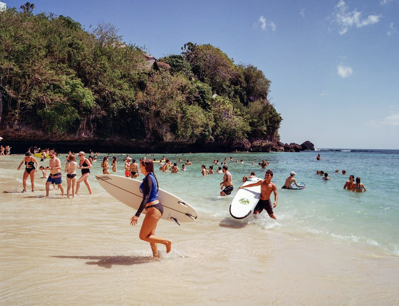 Surfers and swimmers on a small cove beach below a jungle headland
