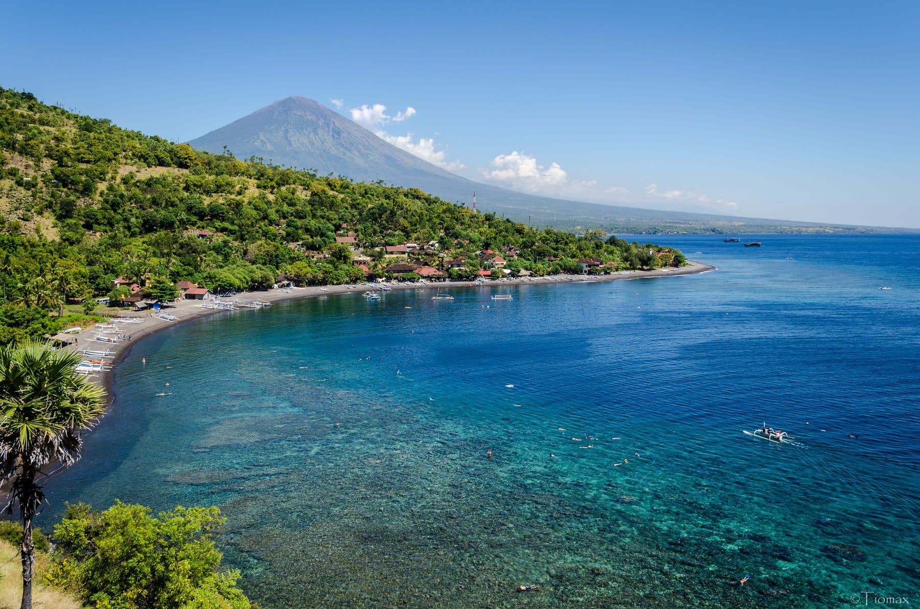 The bay at Amed seen from the hillside, deep blue water along the shore and Mount Agung rising behind the coast