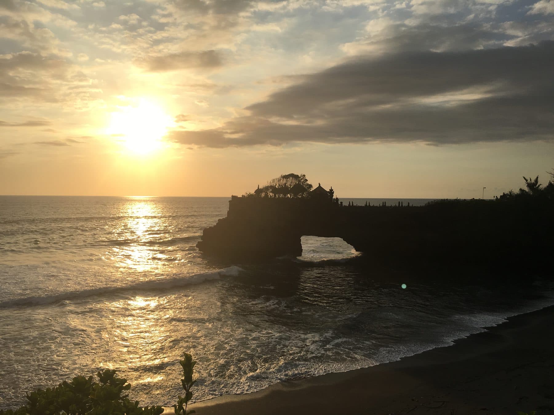 The Batu Bolong temple at Canggu silhouetted on its rock arch, the sun setting behind it over the sea