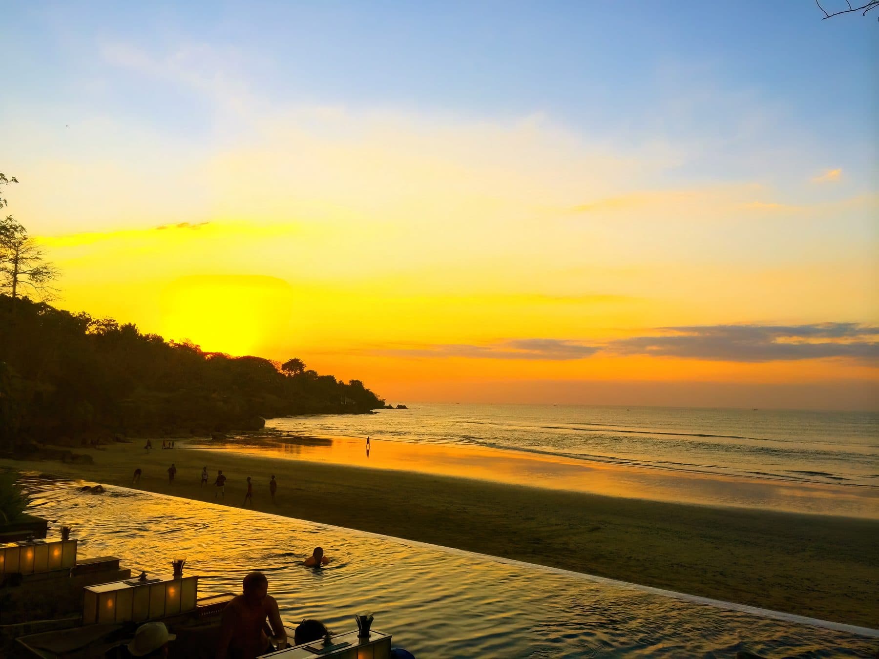 Jimbaran bay at sunset, the sky gold above a long curve of beach and the water reflecting the light