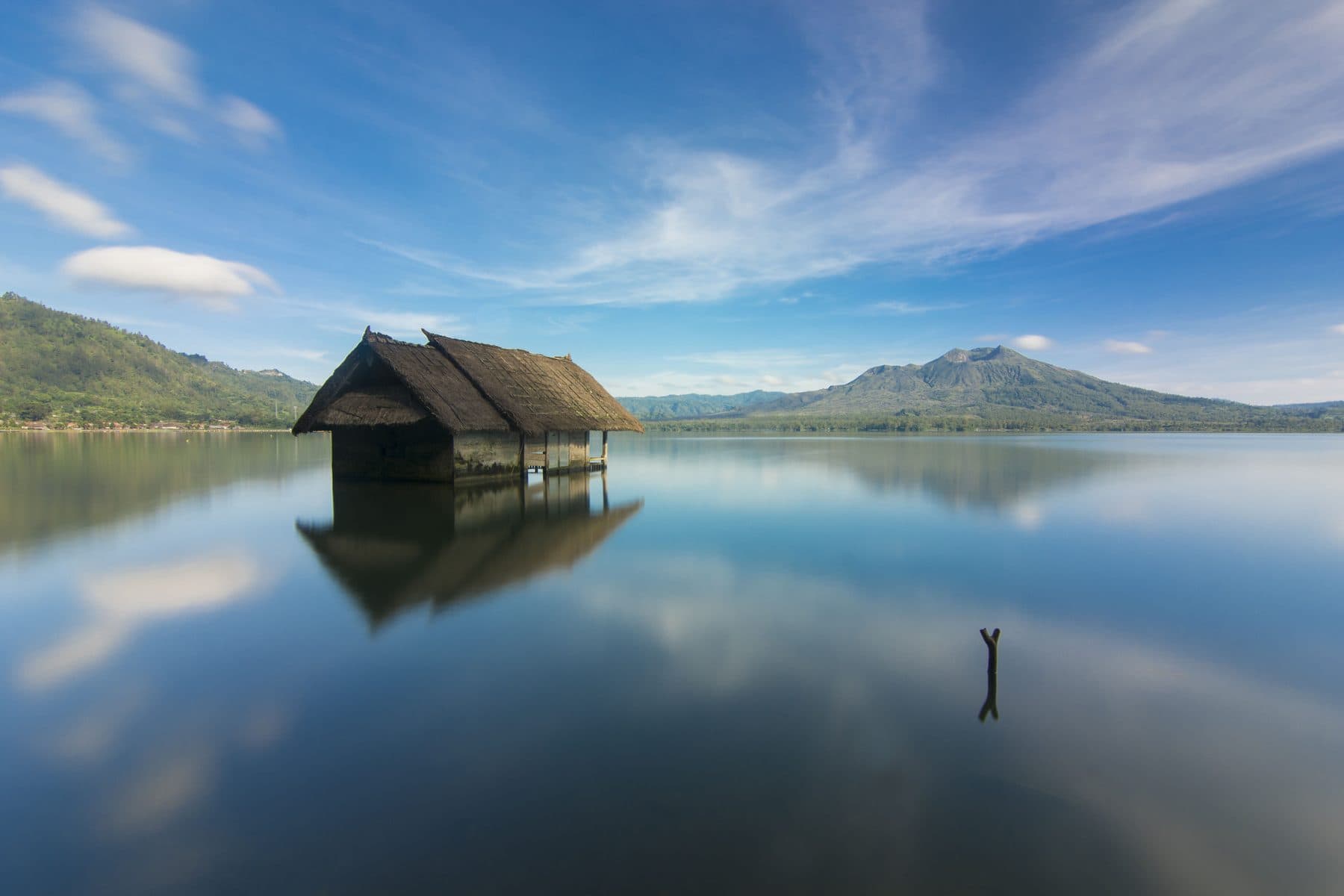 A hut standing on the still water of Lake Batur at Kintamani, the volcano rim reflected behind it