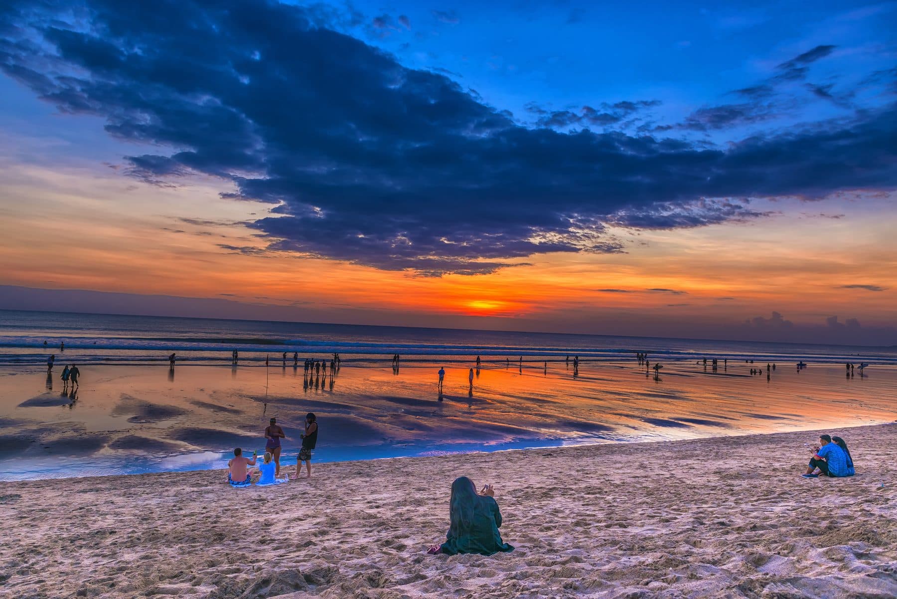 Kuta beach at sunset, the sun low over the sea and small groups of people on the wet sand