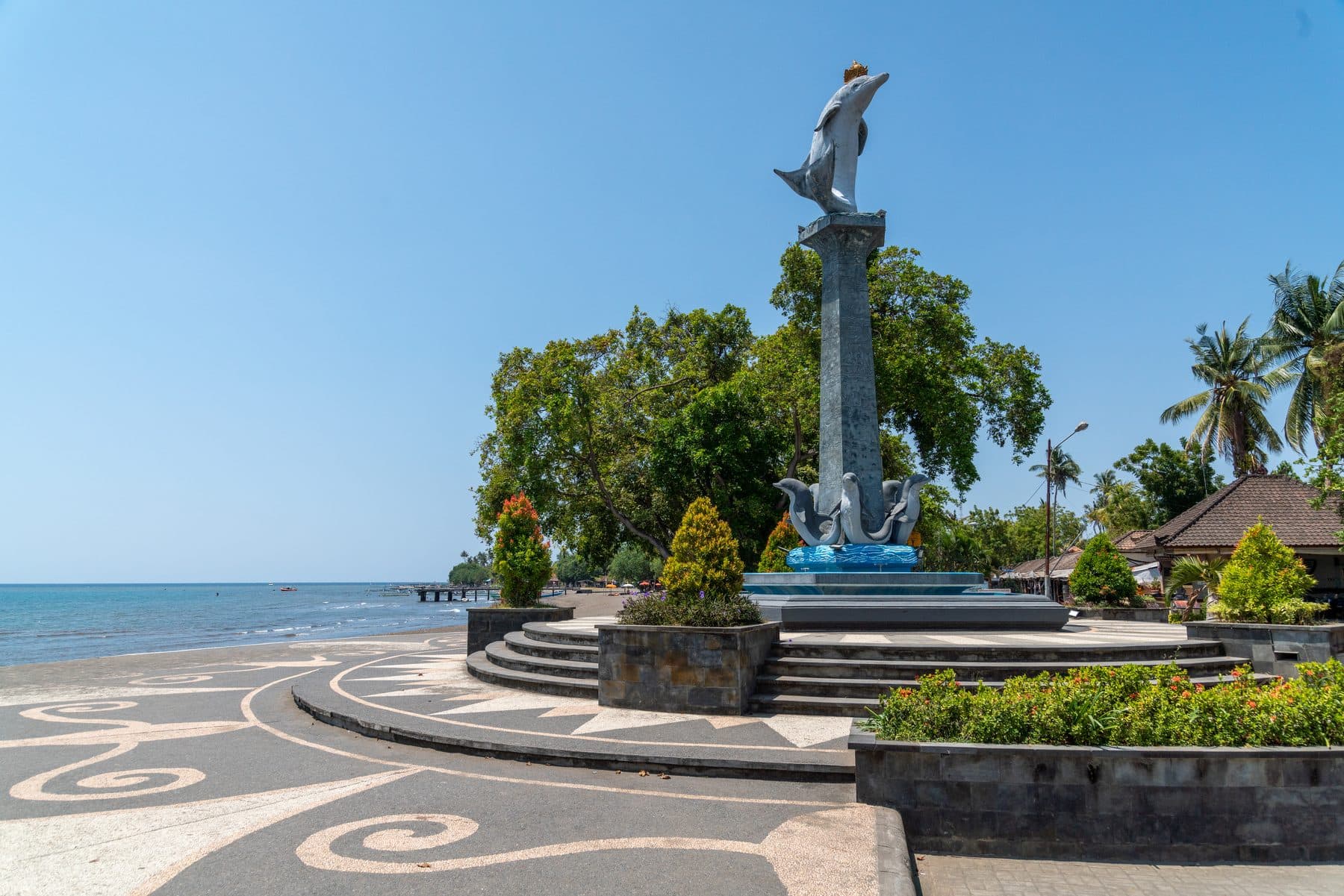 The white dolphin statue that marks the seafront at Lovina, on its plinth against palms and the sea