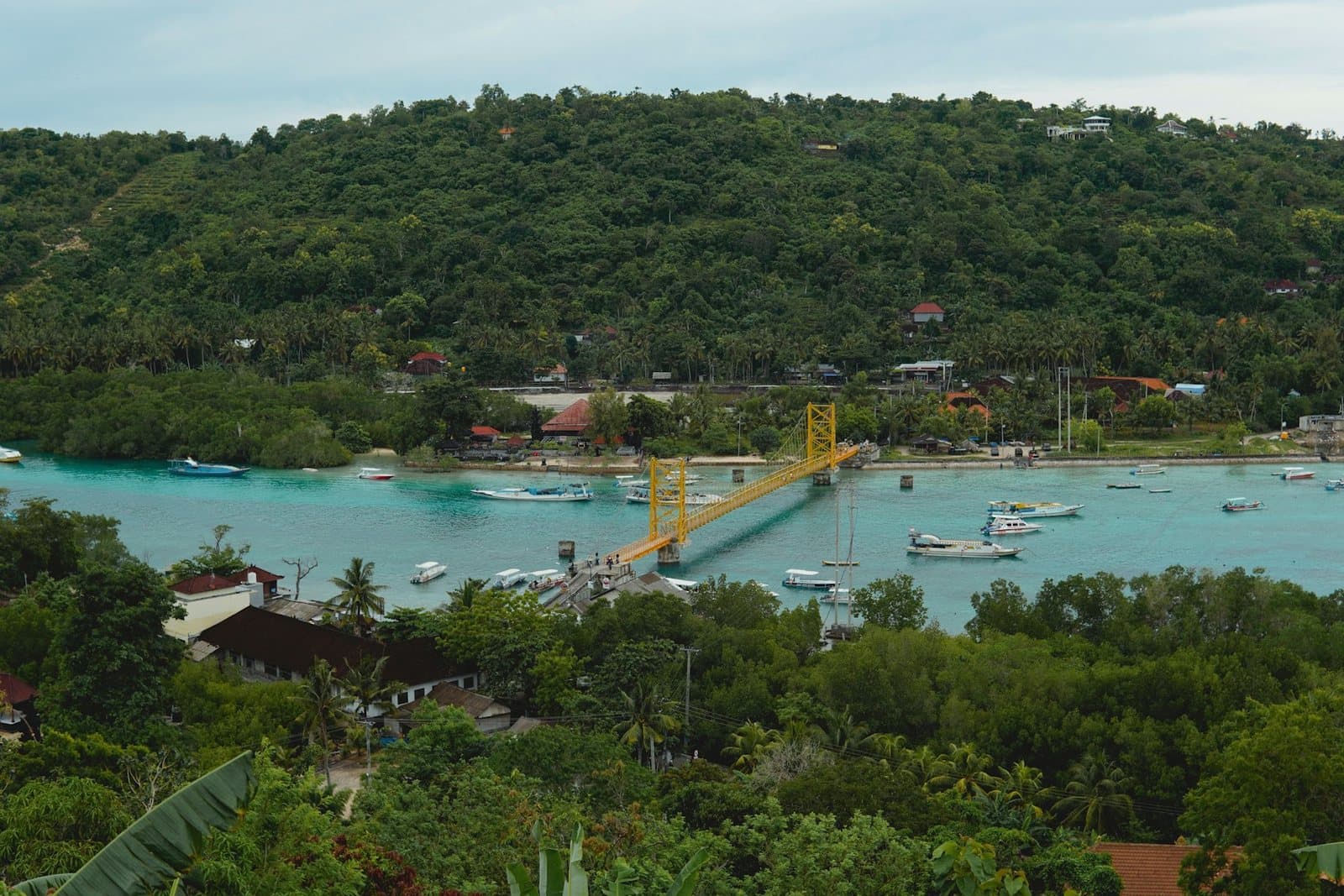 A sheltered island bay with moored boats, mangroves and a yellow bridge crossing to the next island