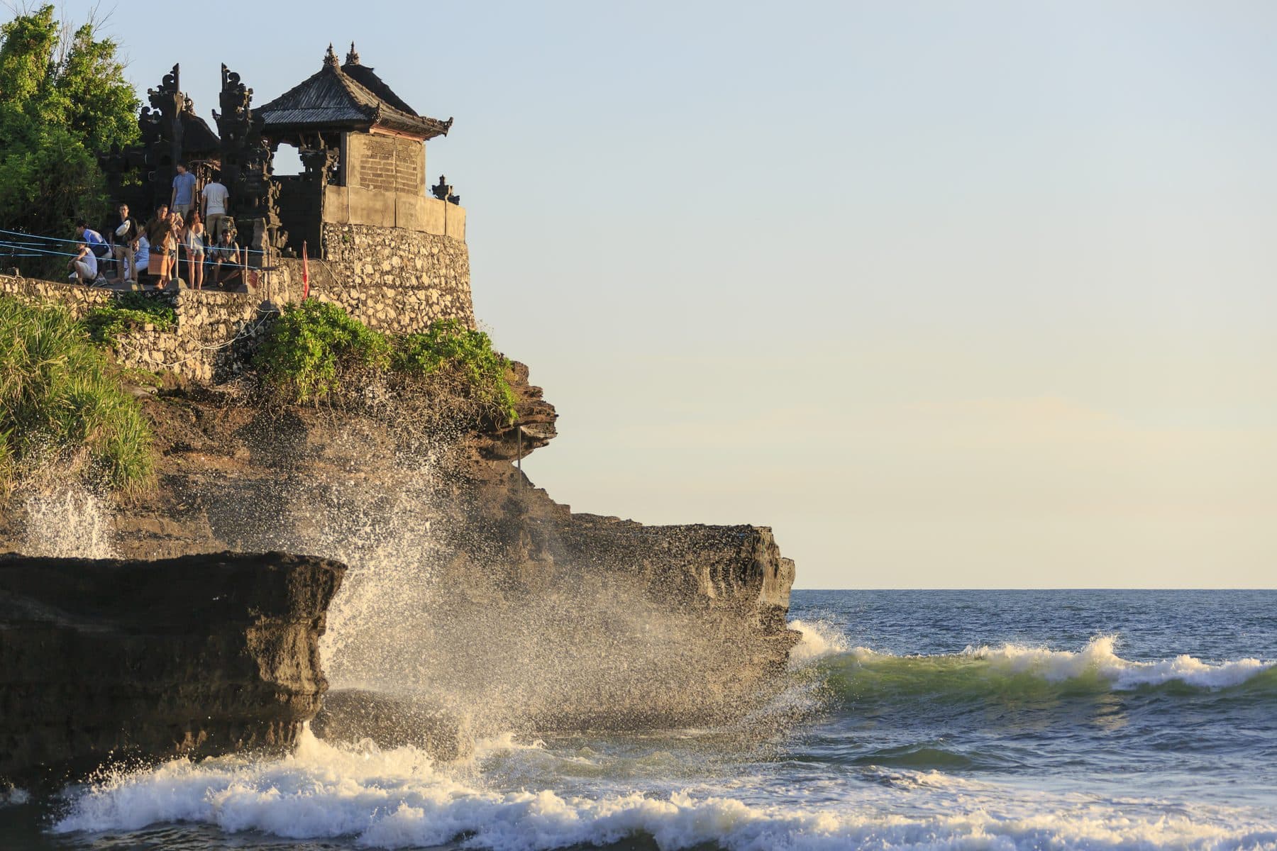 The Tanah Lot temple on its rock, a wave breaking white against the base of the outcrop